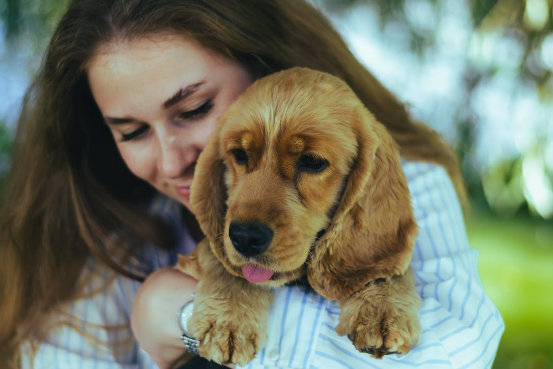 A smiling pet owner cuddling their freshly groomed puppy outdoors.